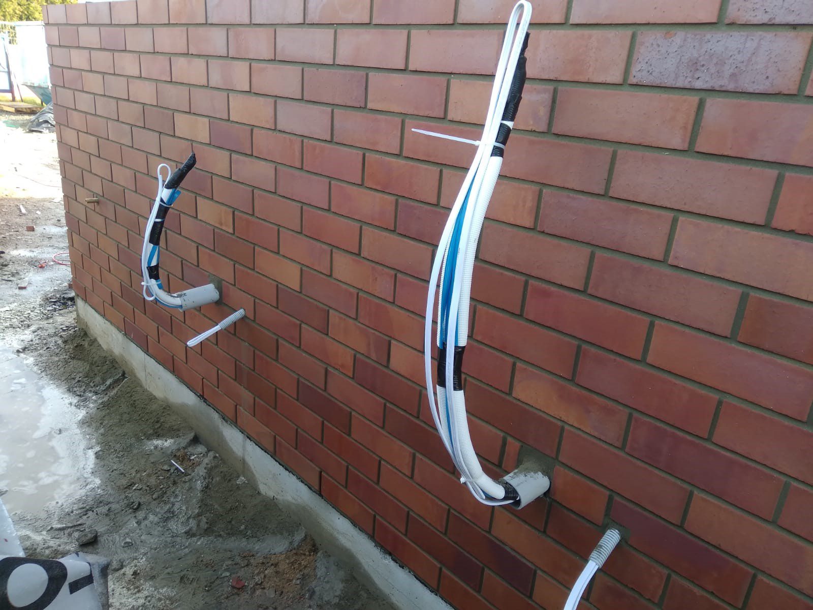 A brick wall with two pipes attached, possibly for air conditioning cables.